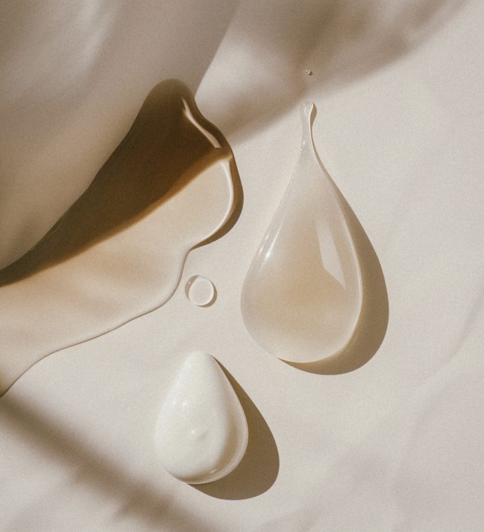 f7767ff7-4acc-4547-bec1-b3cc597951d5 A flat lay of two droplets of cream and oil on an off-white background, with gentle shadows cast in the style of the light source, creating a minimalist aesthetic. The focus is on texture and color contrast between these three elements. Job ID: eea1e021-12d0-4c03-94d2-89b44ae414b0